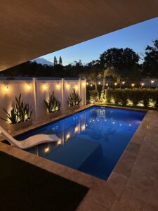 Cozy outdoor pool area illuminated with string lights and lush greenery at dusk.