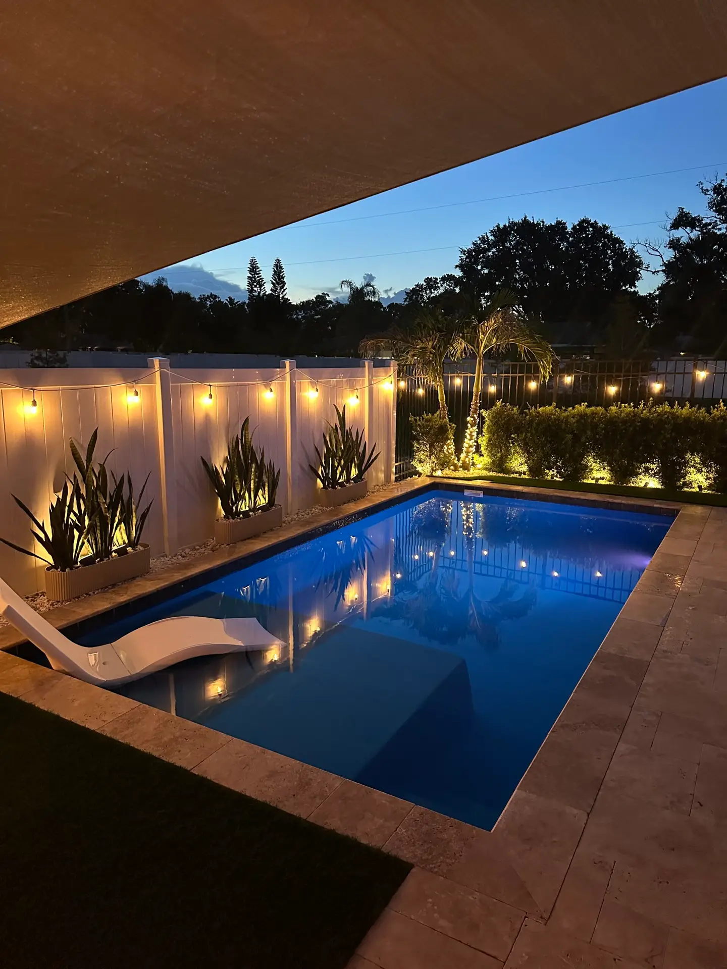 Cozy outdoor pool area illuminated with string lights and lush greenery at dusk.